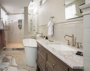 to the right is a dark wood cabinet with a marble top, then a spa like bath tub, then a huge dual shower all with tile floor and half wall